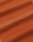 Carpenter Jeans in Burnt Terracotta fabric detail close up. Contrast white topstitching.