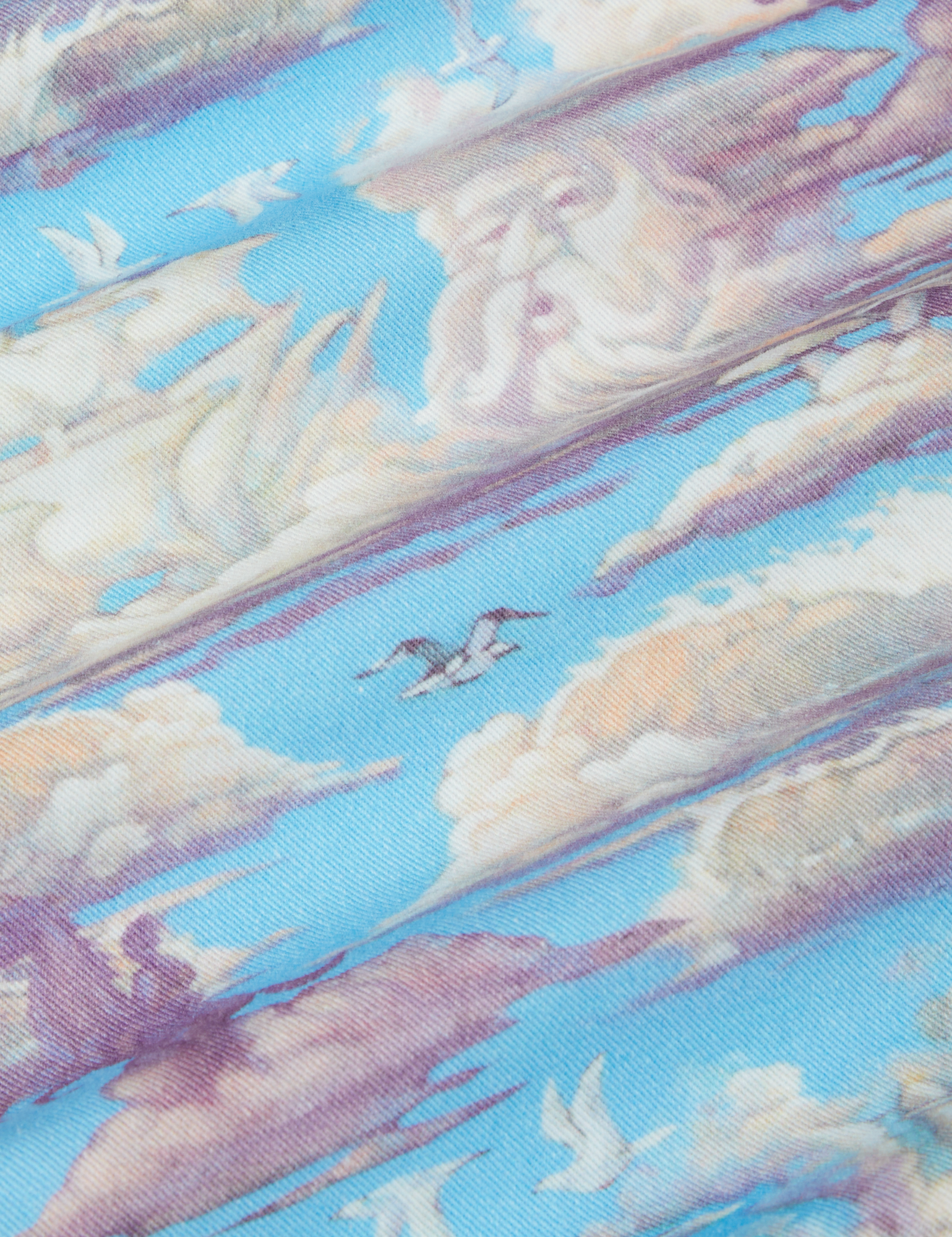 Cloud Kingdom Jumpsuit fabric detail close up. White clouds, birds flying through the sky and a person on a horse.