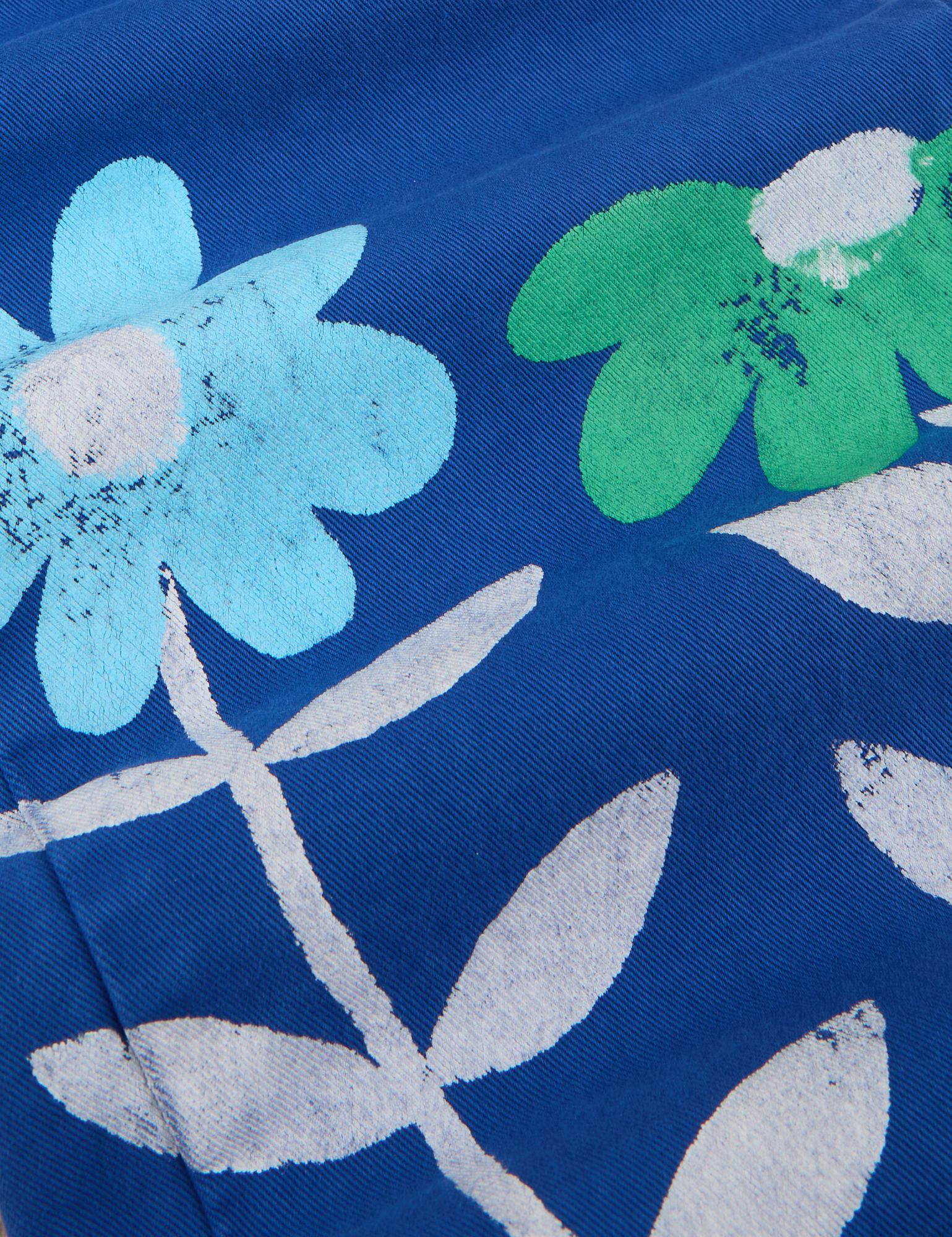 Paintstamped Work Pants in Daisy fabric detail close up. Paintstamped light blue and green daisies with white outline of stem and leaves.