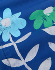 Paintstamped Work Pants in Daisy fabric detail close up. Paintstamped light blue and green daisies with white outline of stem and leaves.