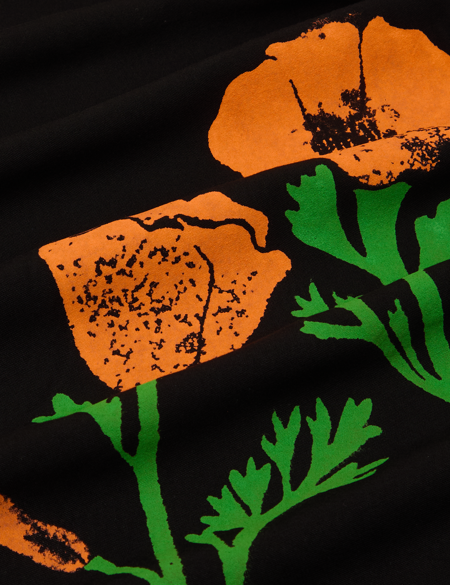 Close up of paintstamped poppies in orange and green on black work pants