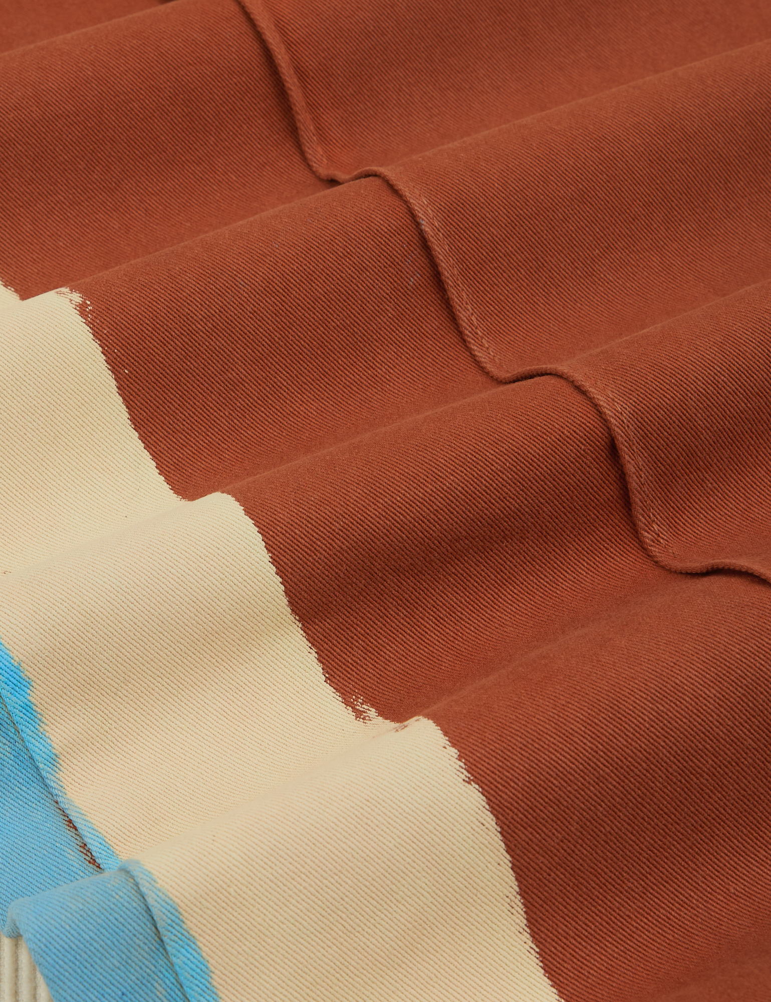 Hand-Painted Stripe Western Pants in Burnt Terracotta fabric detail close up. Painted off-white and light blue stripe