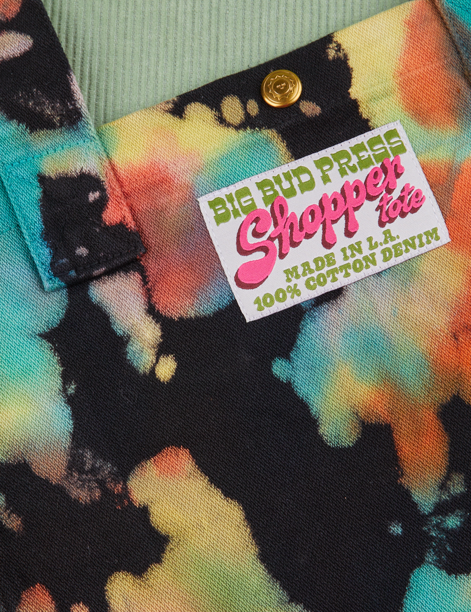 Rainbow Magic Waters Shopper Tote fabric detail close up. Bag label sewn on front that reads 'Big Bud Press' in green, 'Shopper Tote' in pink, 'Made in L.A. 100% Cotton Denim' in green on a white background