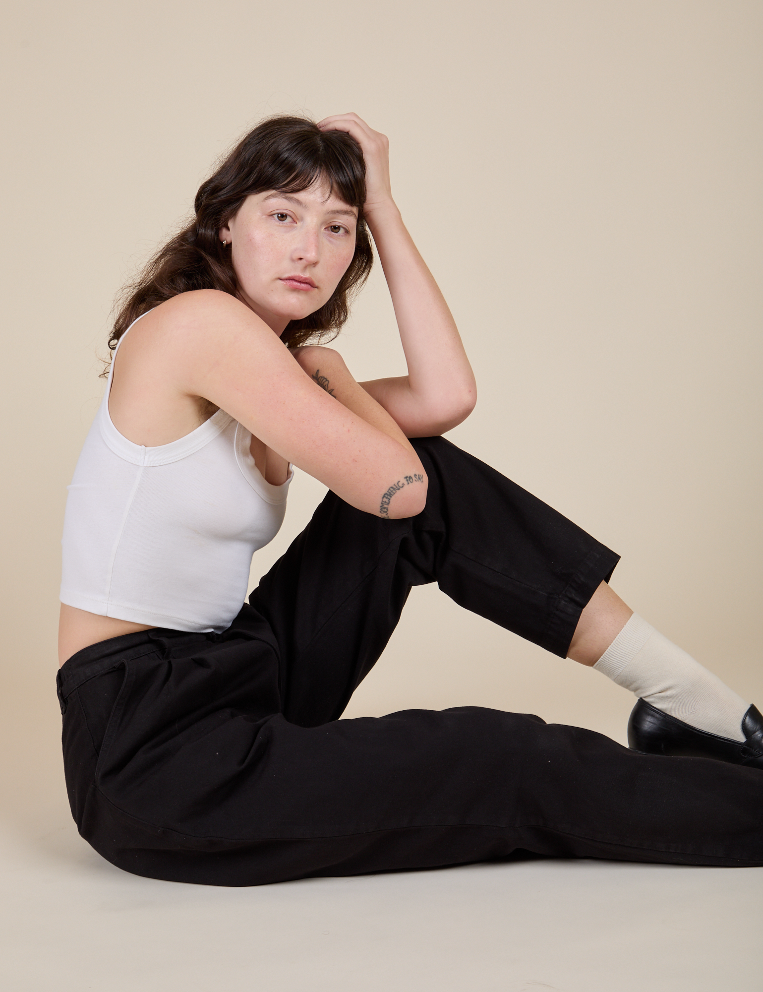 Sitting side view of Heavyweight Trousers in Basic Black and vintage tee white Cropped Tank on Alex