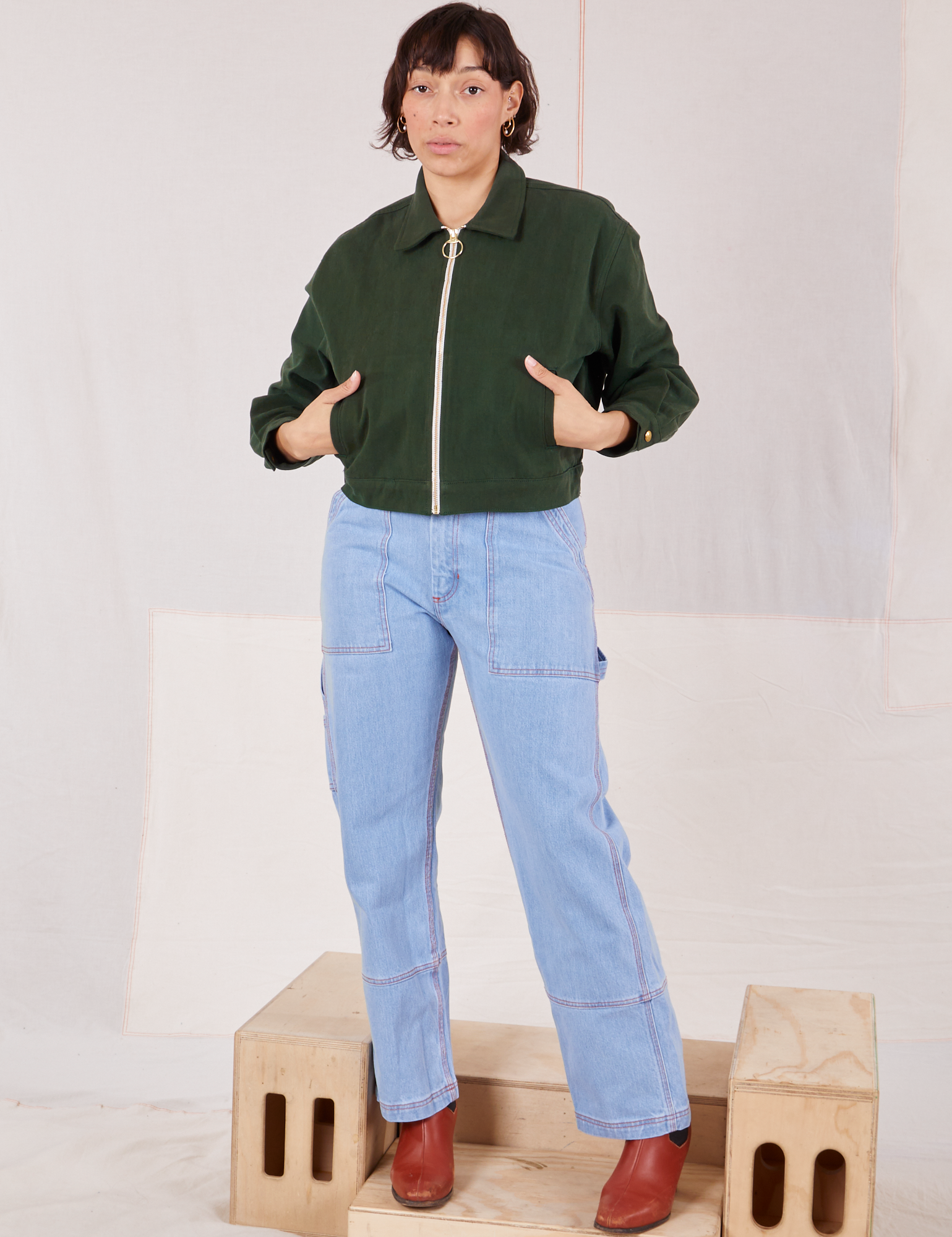 Tiara is wearing a zipped up Ricky Jacket in Swamp Green and light wash Carpenter Jeans