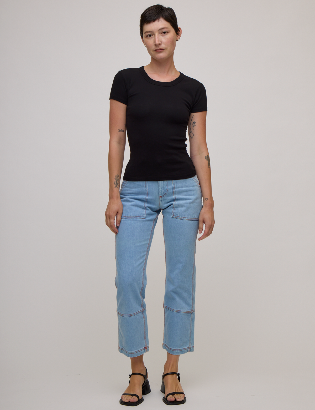 Alex is wearing  Baby Tee in Basic Black and light wash carpenter jeans