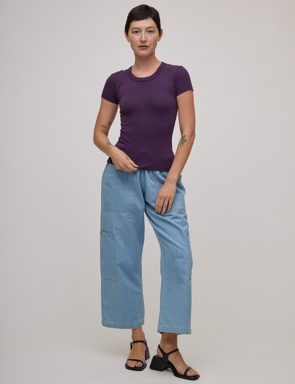 Alex is wearing Baby Tee in Nebula Purple and light wash denim drop pocket pants