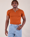 Isaac is wearing Baby Tee in Burnt Terracotta tucked into light wash Denim Trousers