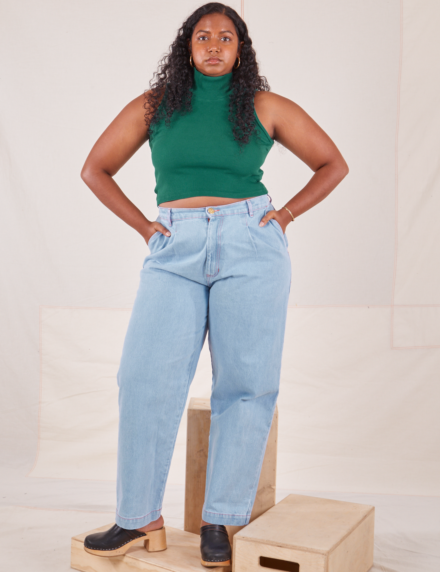 Meghna is 5'8" and wearing XS Sleeveless Essential Turtleneck in Hunter Green paired with light wash Denim Trousers
