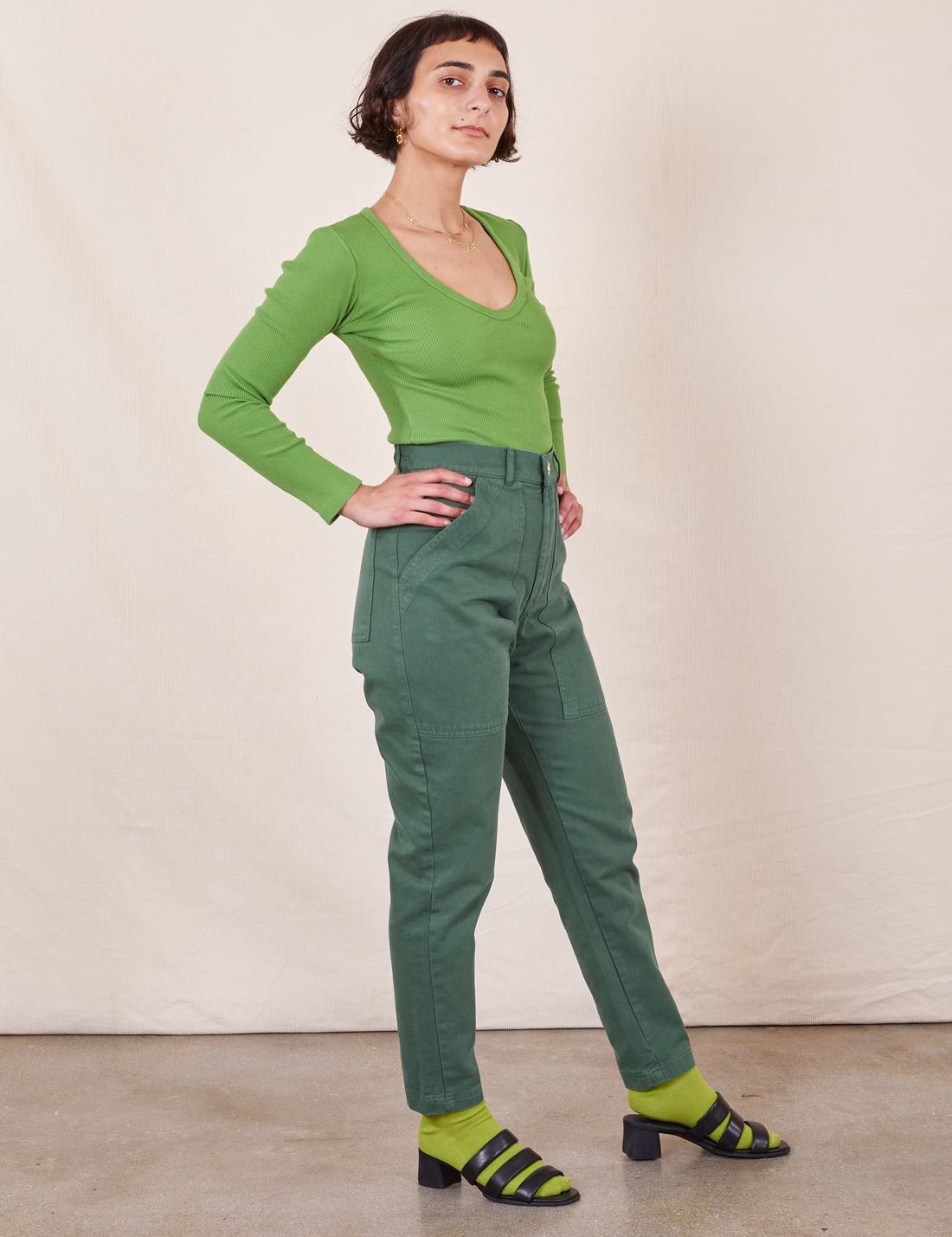 Side view of Pencil Pants in Dark Emerald Green paired with a bright green Long Sleeve V-Neck Tee worn by Soraya