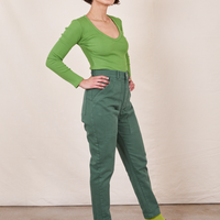 Side view of Pencil Pants in Dark Emerald Green paired with a bright green Long Sleeve V-Neck Tee worn by Soraya
