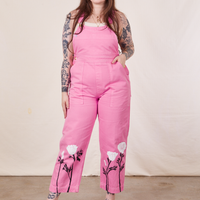 Sydney is wearing California Poppy Overalls in Bubblegum Pink with a vintage off-white Tank Top underneath. She has her right hand on the side and her left hand tucked into the pocket.
