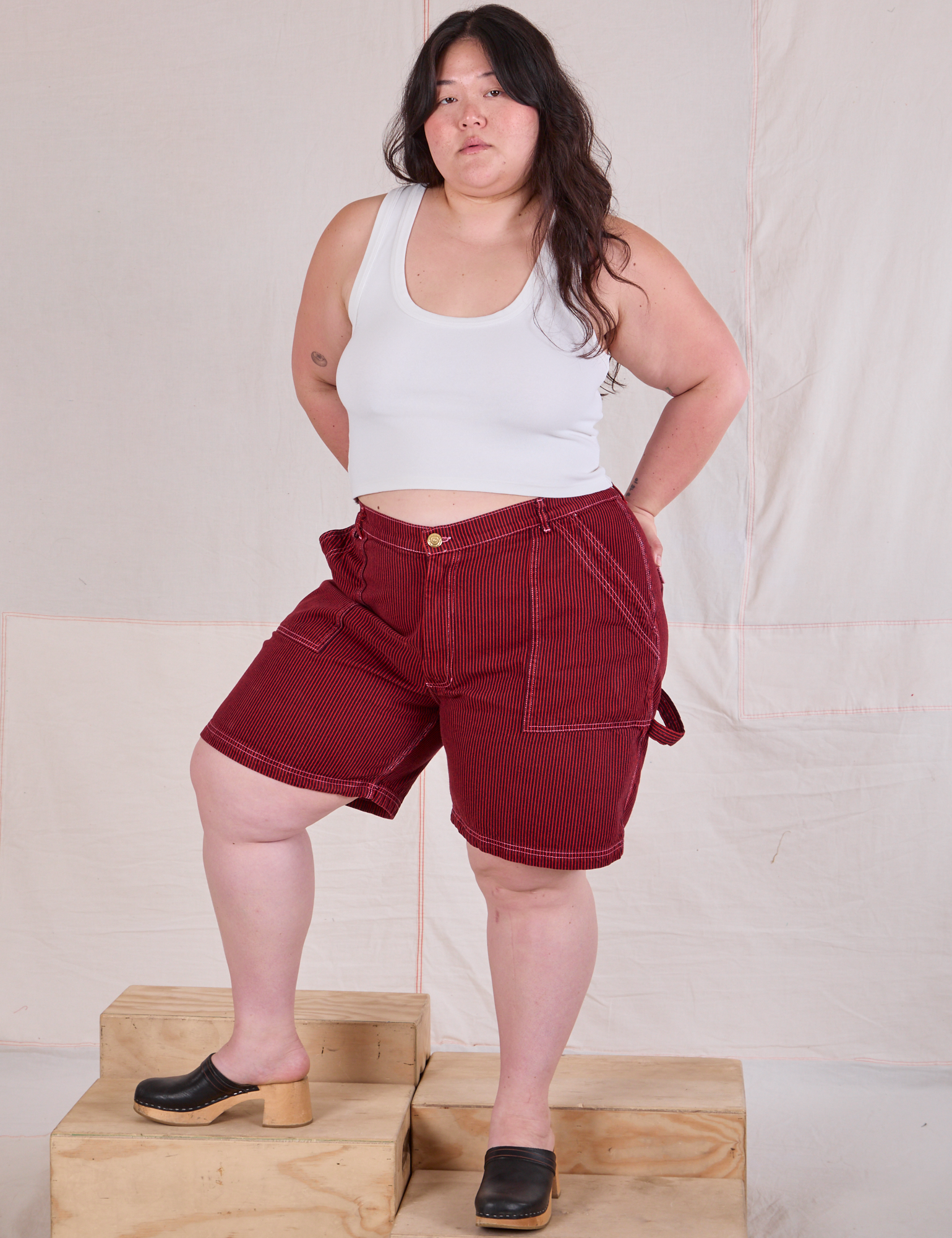 Ashley is wearing Railroad Carpenter Shorts in Mustang Red and a Cropped Tank in Vintage Tee Off-White
