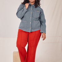 Railroad Stripe Denim Work Jacket and paprika Western Pants worn by Morgan. The jacket is buttoned up and Morgan is holding the point of the collar.