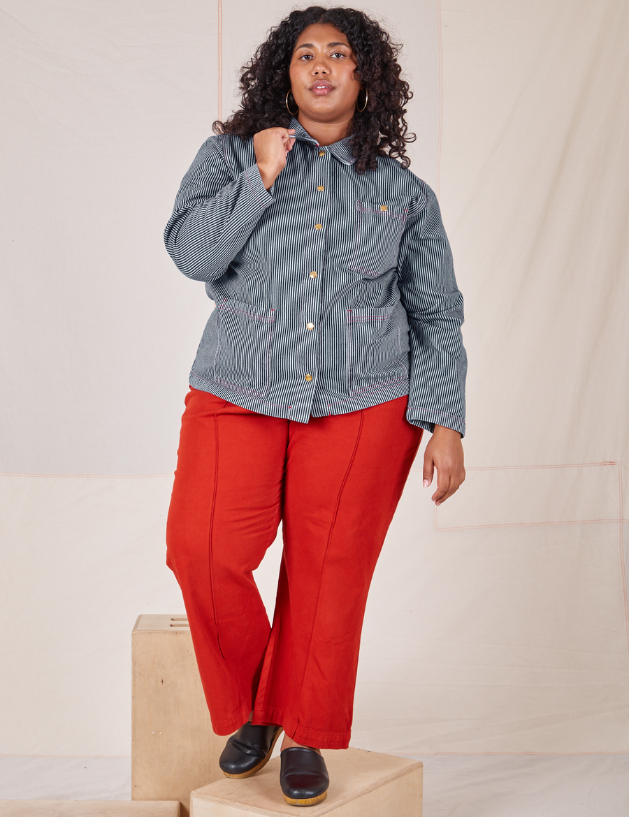 Railroad Stripe Denim Work Jacket and paprika Western Pants worn by Morgan. The jacket is buttoned up and Morgan is holding the point of the collar.