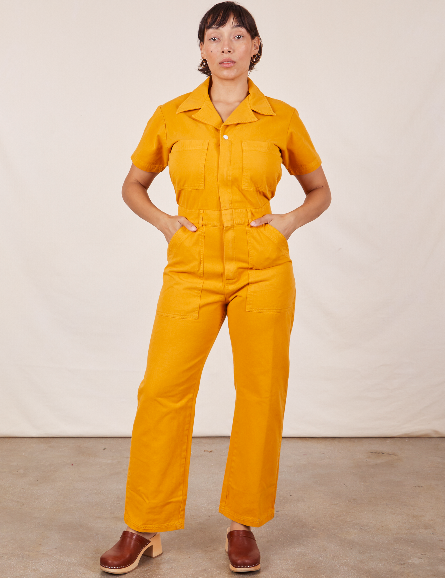 Tiara is 5'4" and wearing S Short Sleeve Jumpsuit in Mustard Yellow