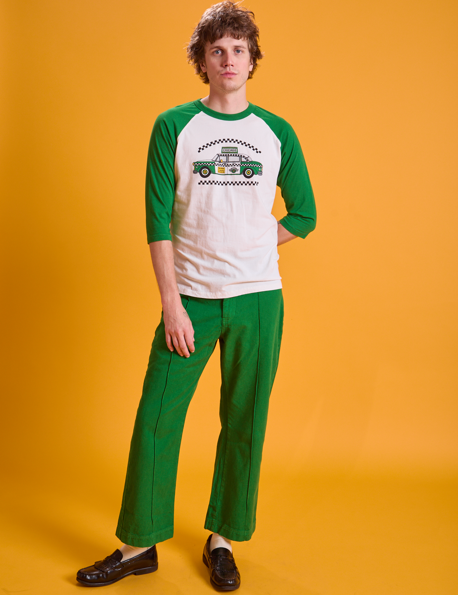Quinn is wearing Taxi Raglan Tee in Chicago and forest green Western Pants