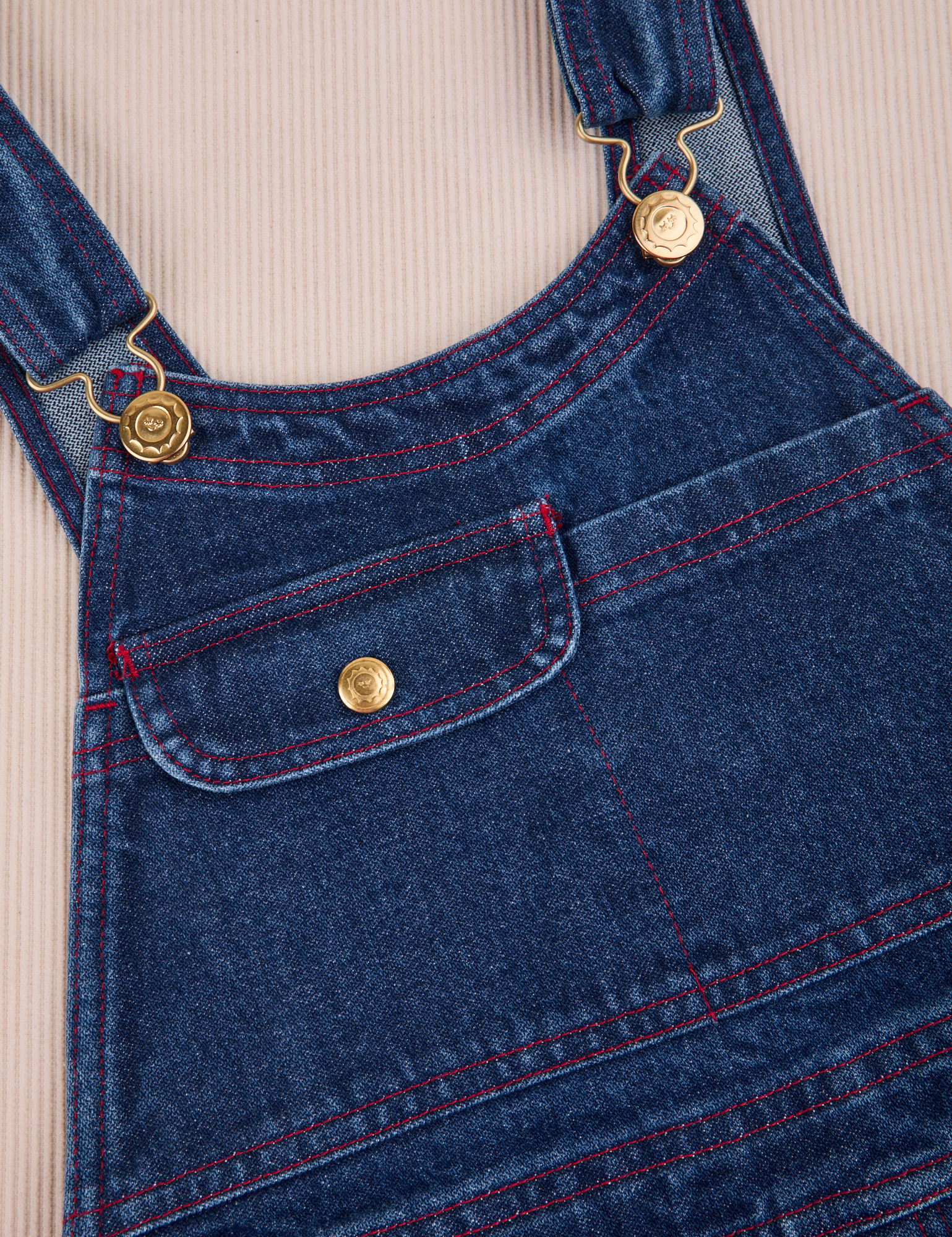 Carpenter Overalls in Dark Wash front close up. Contrast red top stitching and brass details.