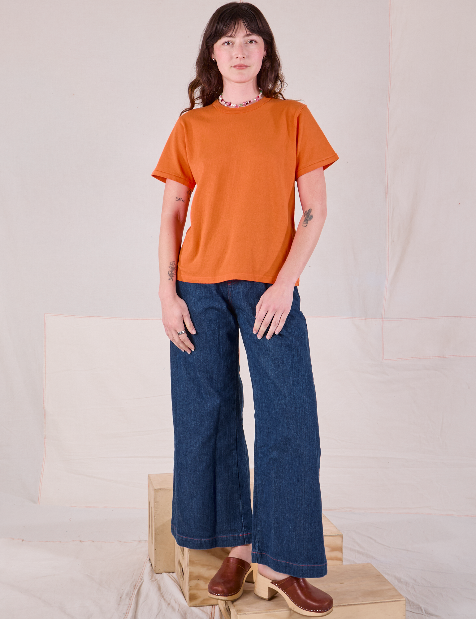 Alex is wearing Burly Tee in Construction Orange and dark wash Denim Wide Leg Trousers