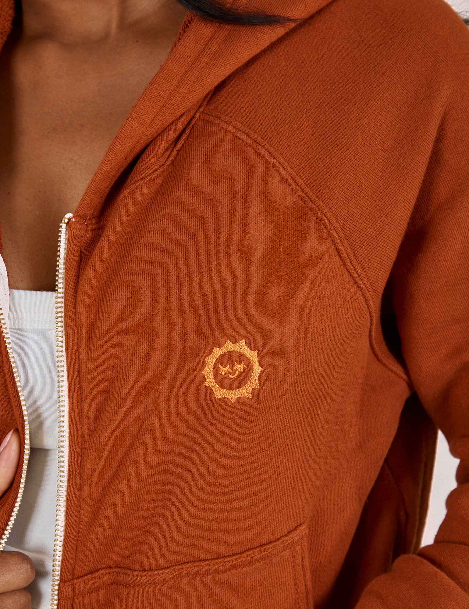 Cropped Zip Hoodie in Burnt Terracotta fabric close up of tonal embroidered sun baby logo