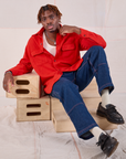 Flannel Overshirt in Mustang Red and dark wash Carpenter Jeans worn by Isaac sitting on a wooden box.