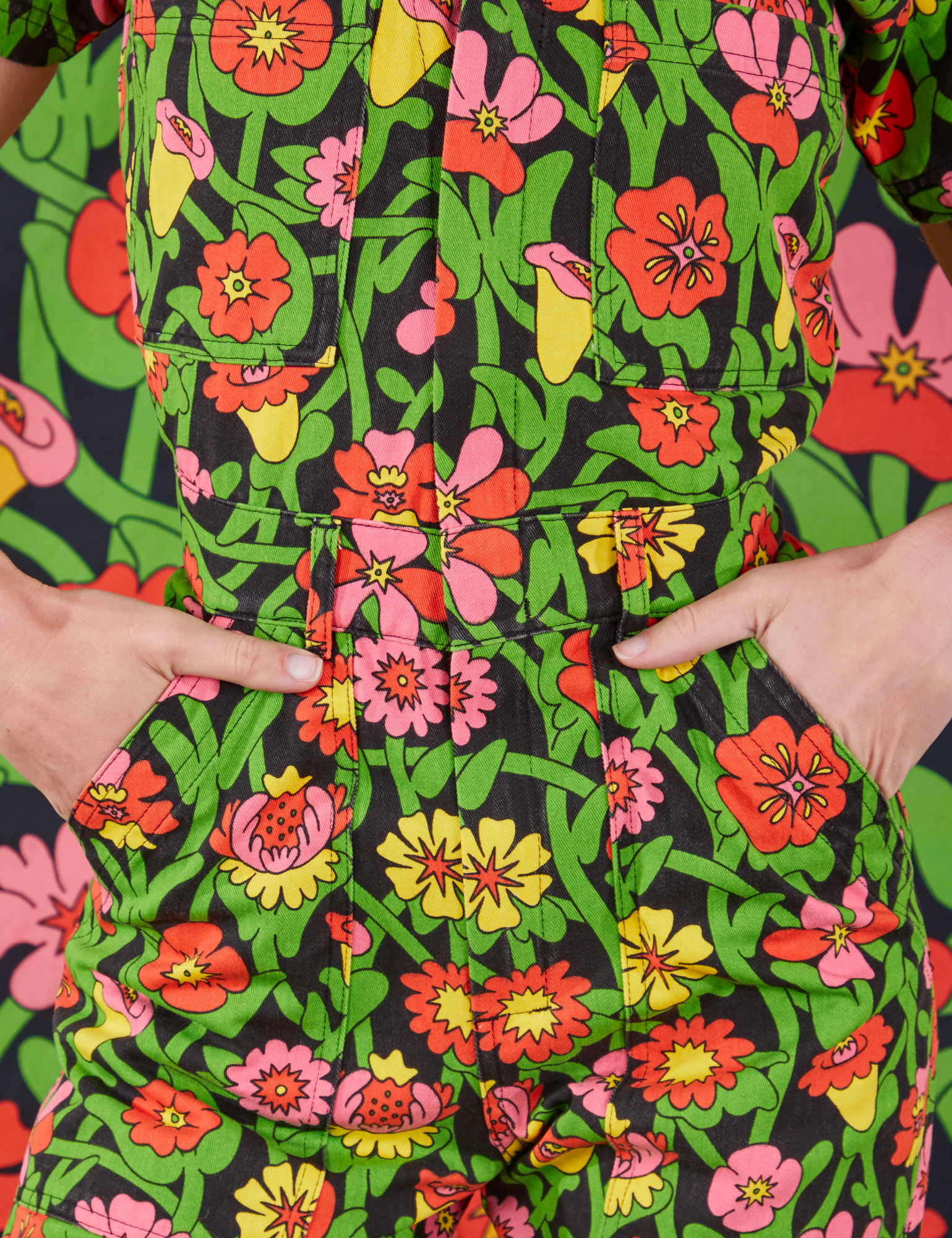 Front close up of Flower Tangle Jumpsuit. Alex has both hands in the pockets.