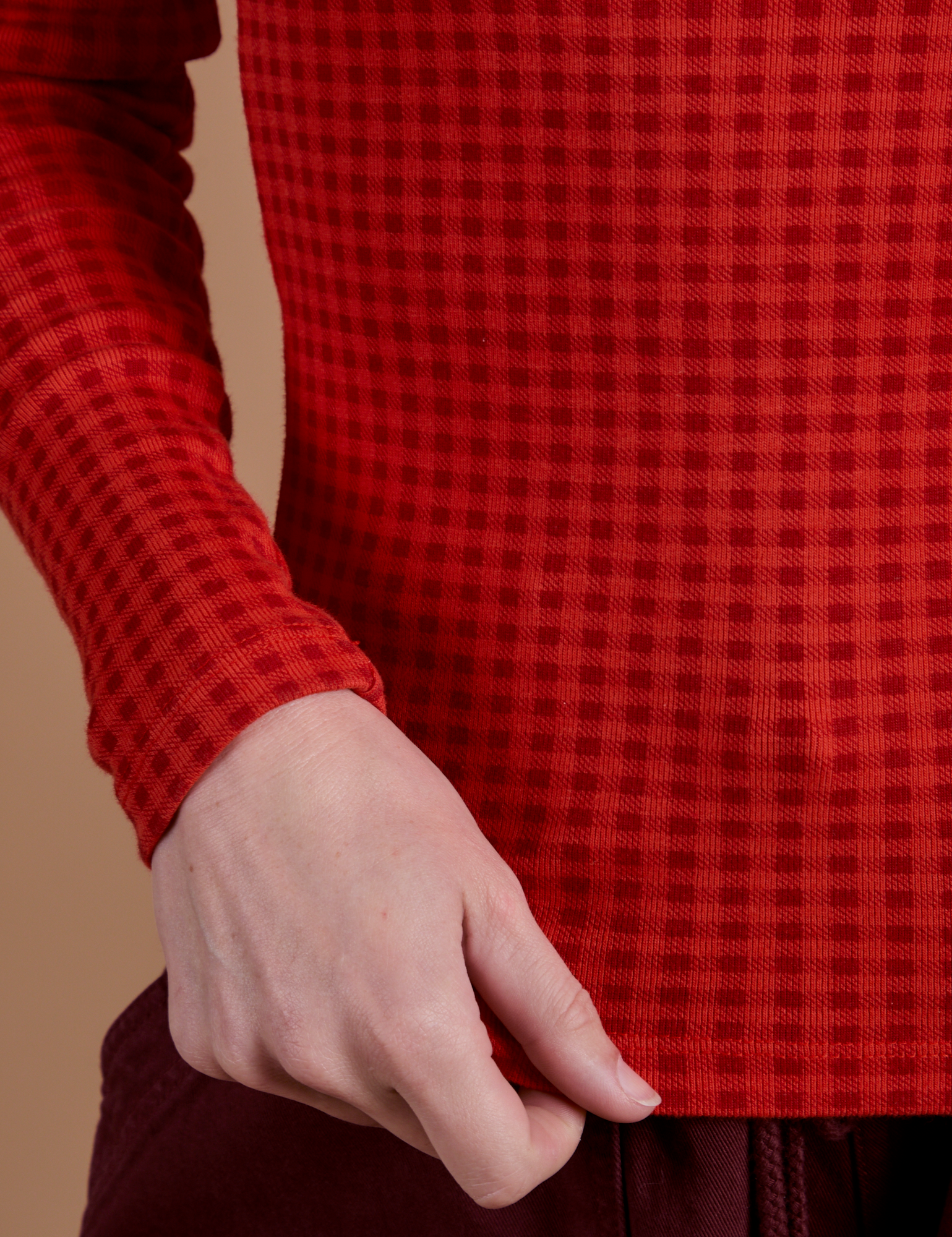 Bottom close up of Gingham Long Sleeve Baby Tee in Mustang Red with Alex holding the hem