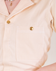 Front close up of Heritage Short Sleeve Jumpsuit in natural worn by Alex. Front pocket features the sun baby brass snap.