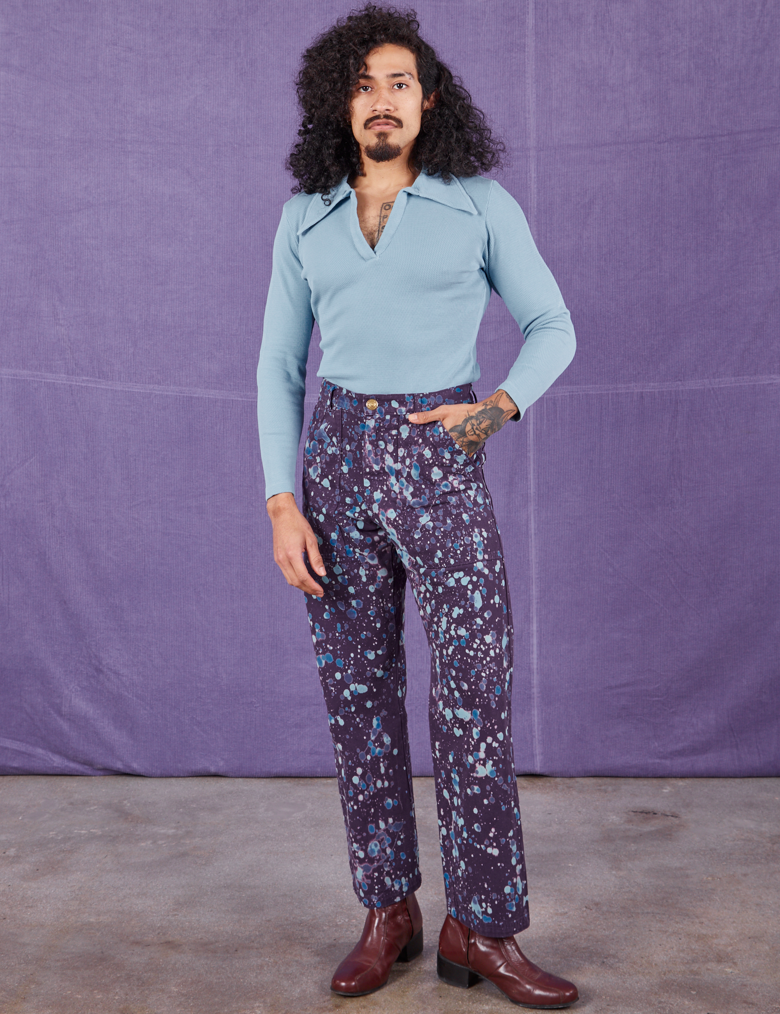 Jesse is wearing Marble Splatter Work Pants in Nebula Purple and baby blue Long Sleeve Fisherman Polo