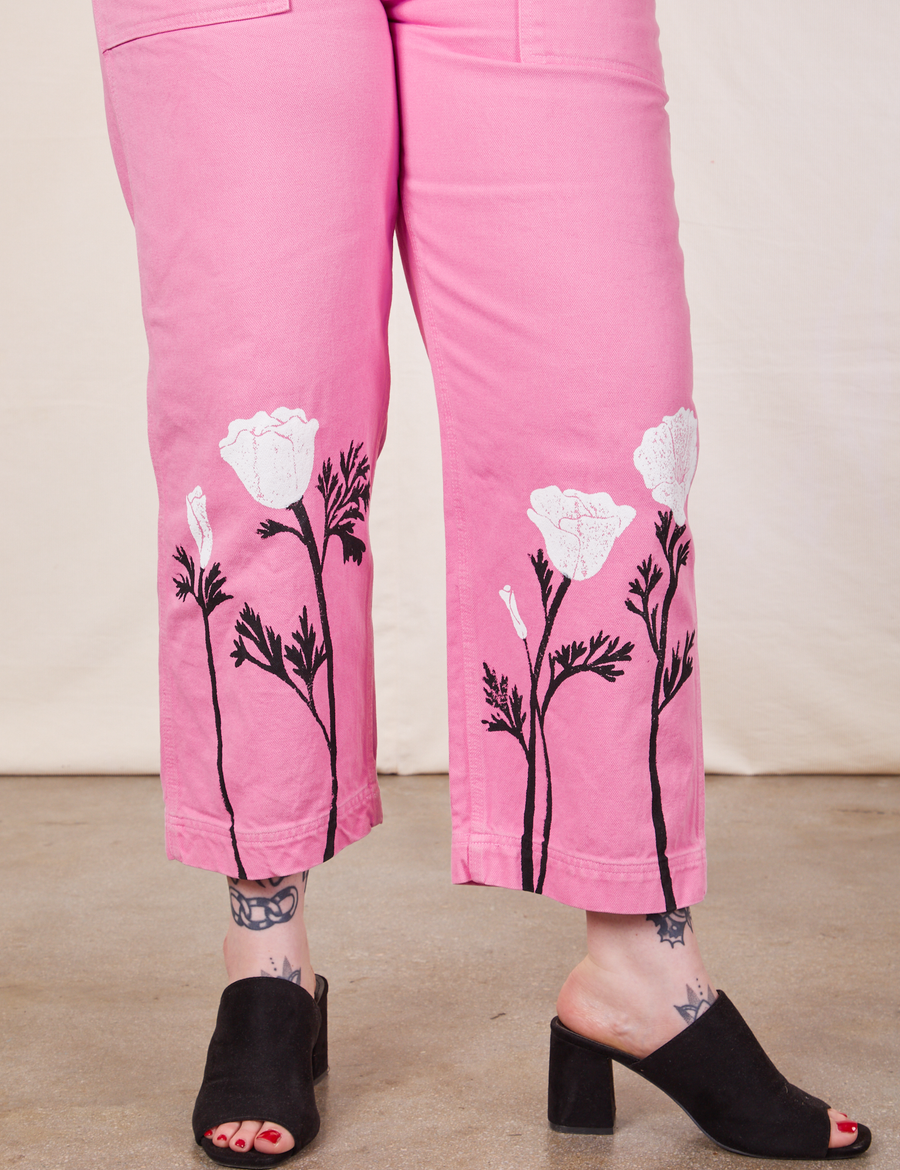Pant leg close up of California Poppy Overalls in Bubblegum Pink. Paintstamped white poppies with black stems and leaves along the bottom of pant.