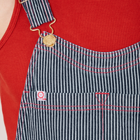 Front close up of Railroad Stripe Denim Original Overalls. Red contrast stitching and white and red sun baby tag.