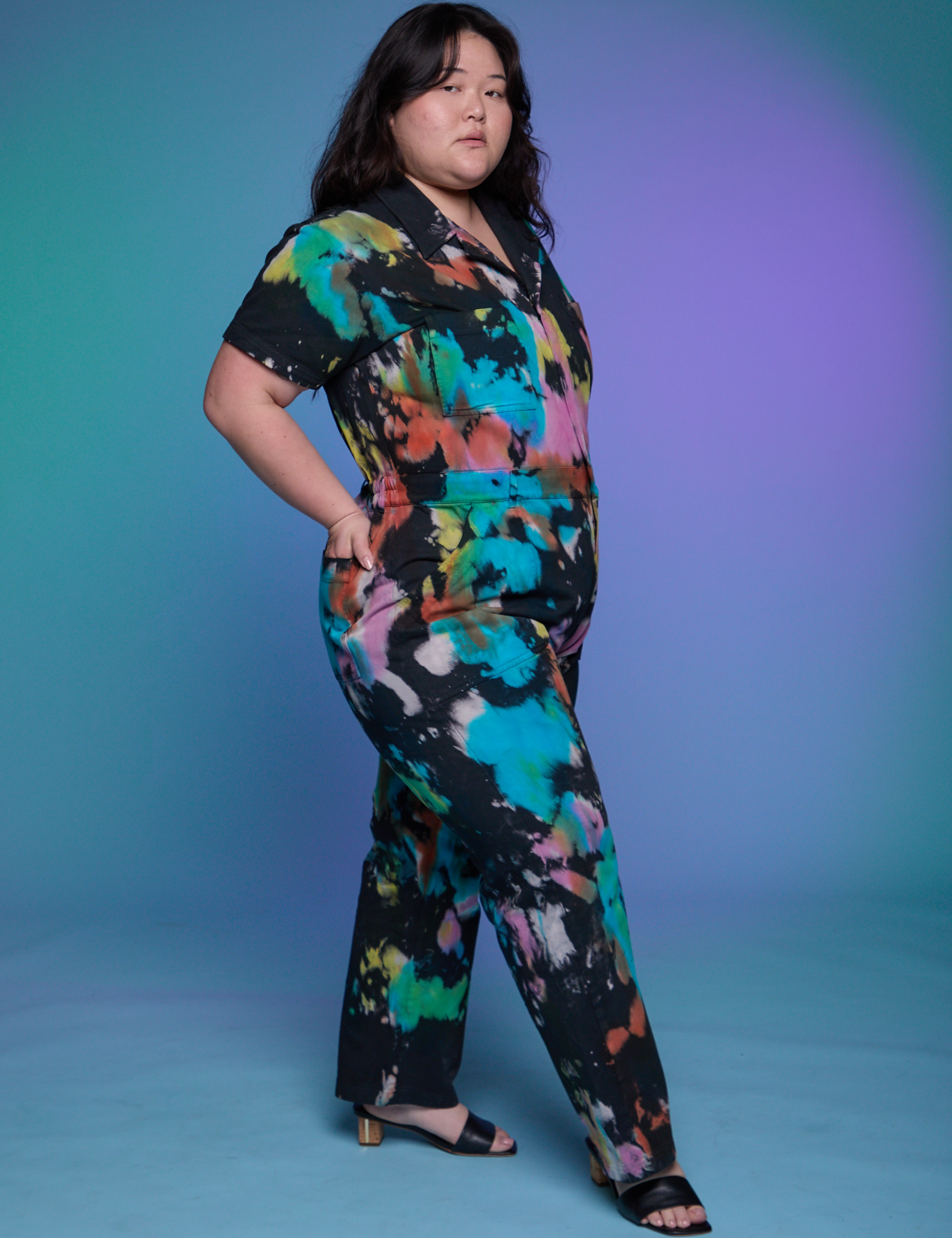 Angled front view of Short Sleeve Jumpsuit in Rainbow Magic Waters on Ashley.