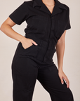 Front close up of Short Sleeve Jumpsuit in Basic Black. Tiara has her hand in the front pocket.