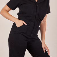 Front close up of Short Sleeve Jumpsuit in Basic Black. Tiara has her hand in the front pocket.