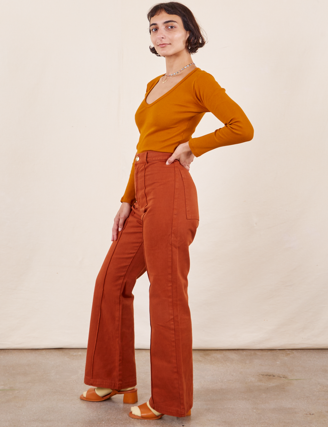 Side view of Western Pants in Burnt Terracotta paired with a burnt orange Long Sleeve V-Neck Tee worn by Soraya