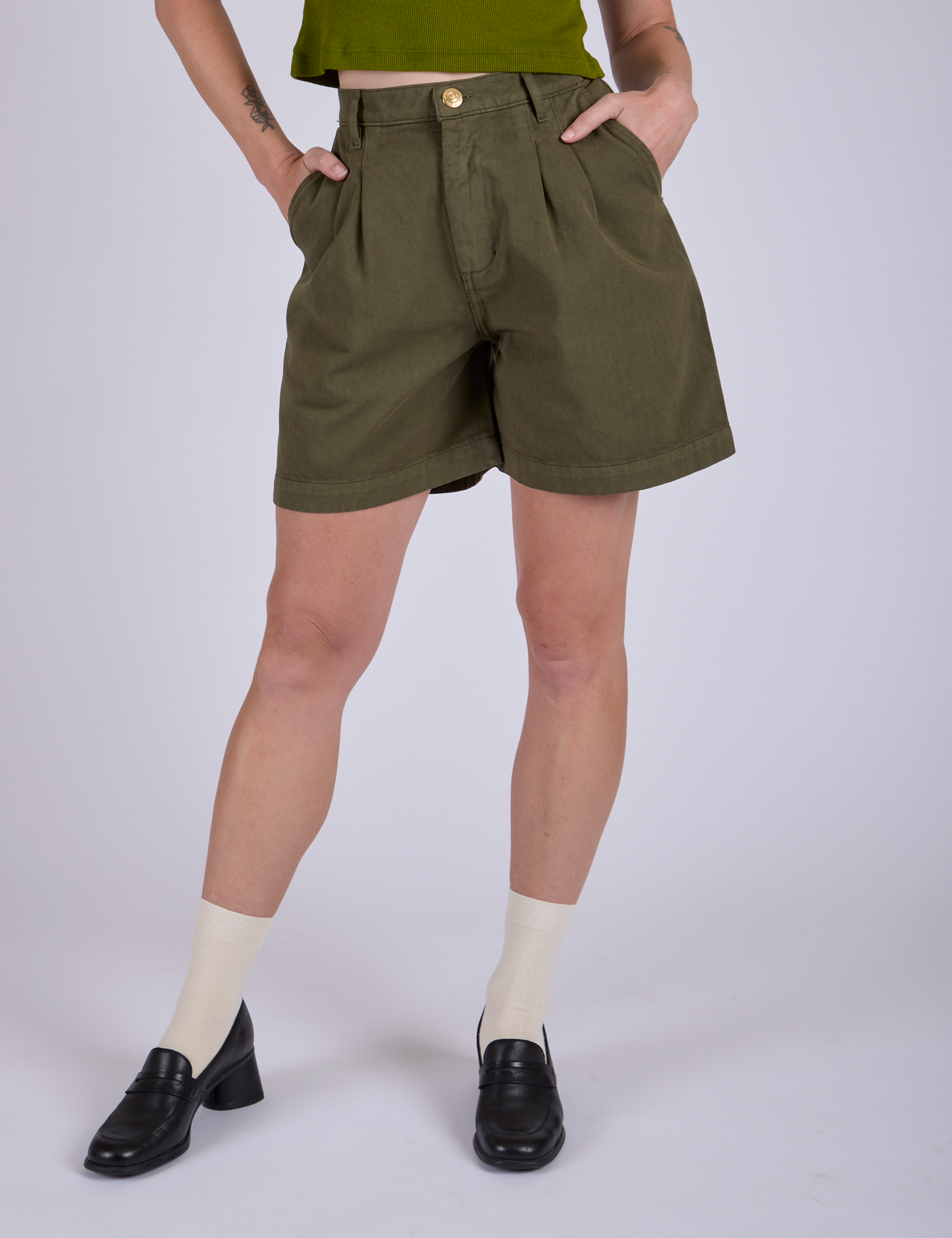 Close up of Pleated Trouser Shorts in Surplus Green with Alex's hands in both front pockets.