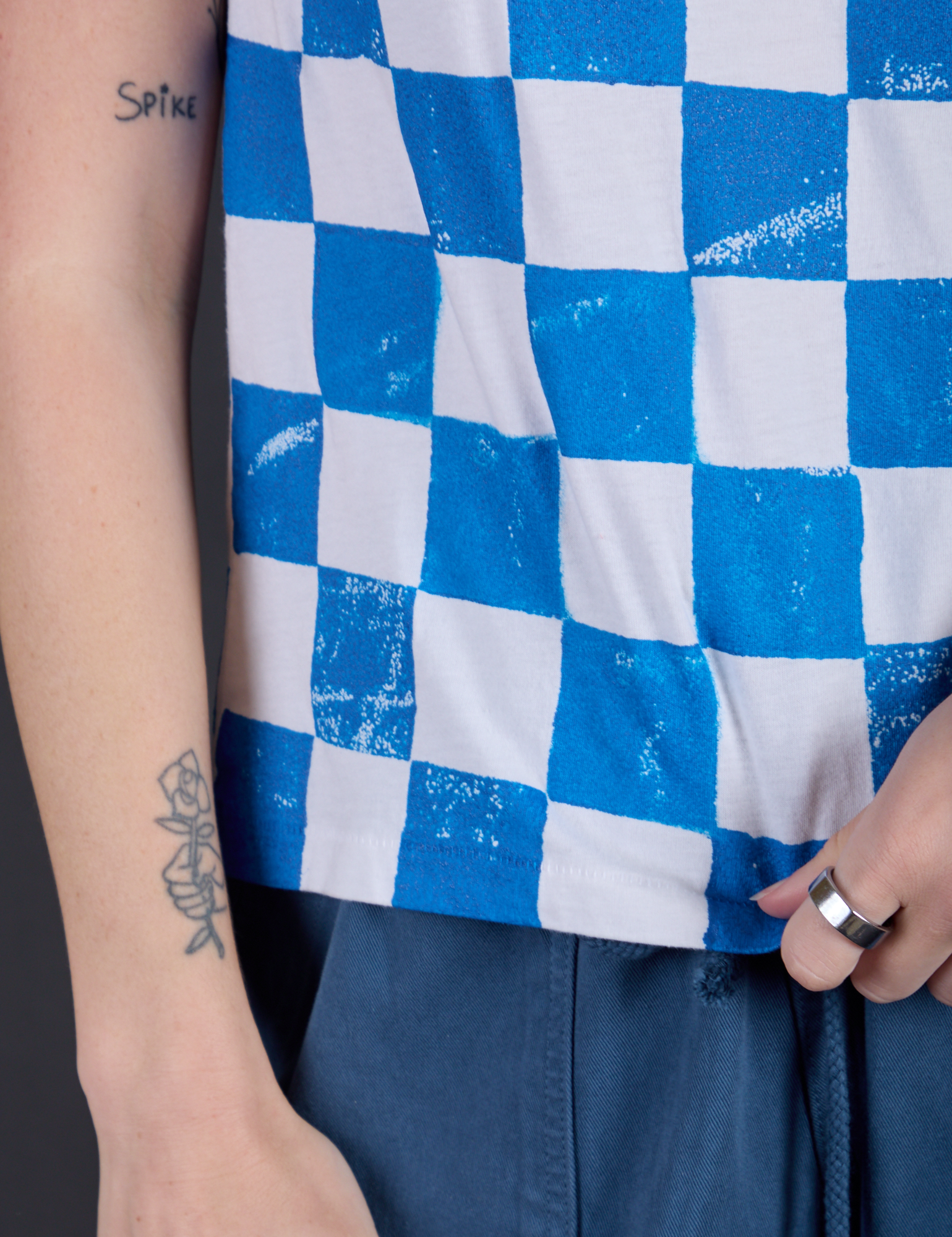 Checker Organic Tee in Blue bottom close up with Alex holding the hem