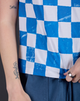 Checker Organic Tee in Blue bottom close up with Alex holding the hem