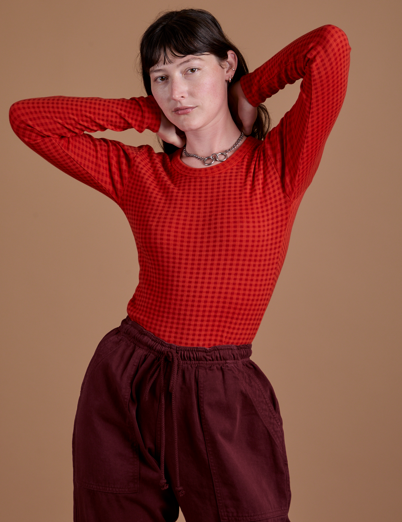 Alex is wearing Gingham Long Sleeve Baby Tee in Mustang Red tucked into red wine Drop Pocket Cargo Pants