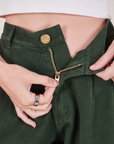 Alex is holding the zipper tab down on the Heritage Trousers in Swamp Green
