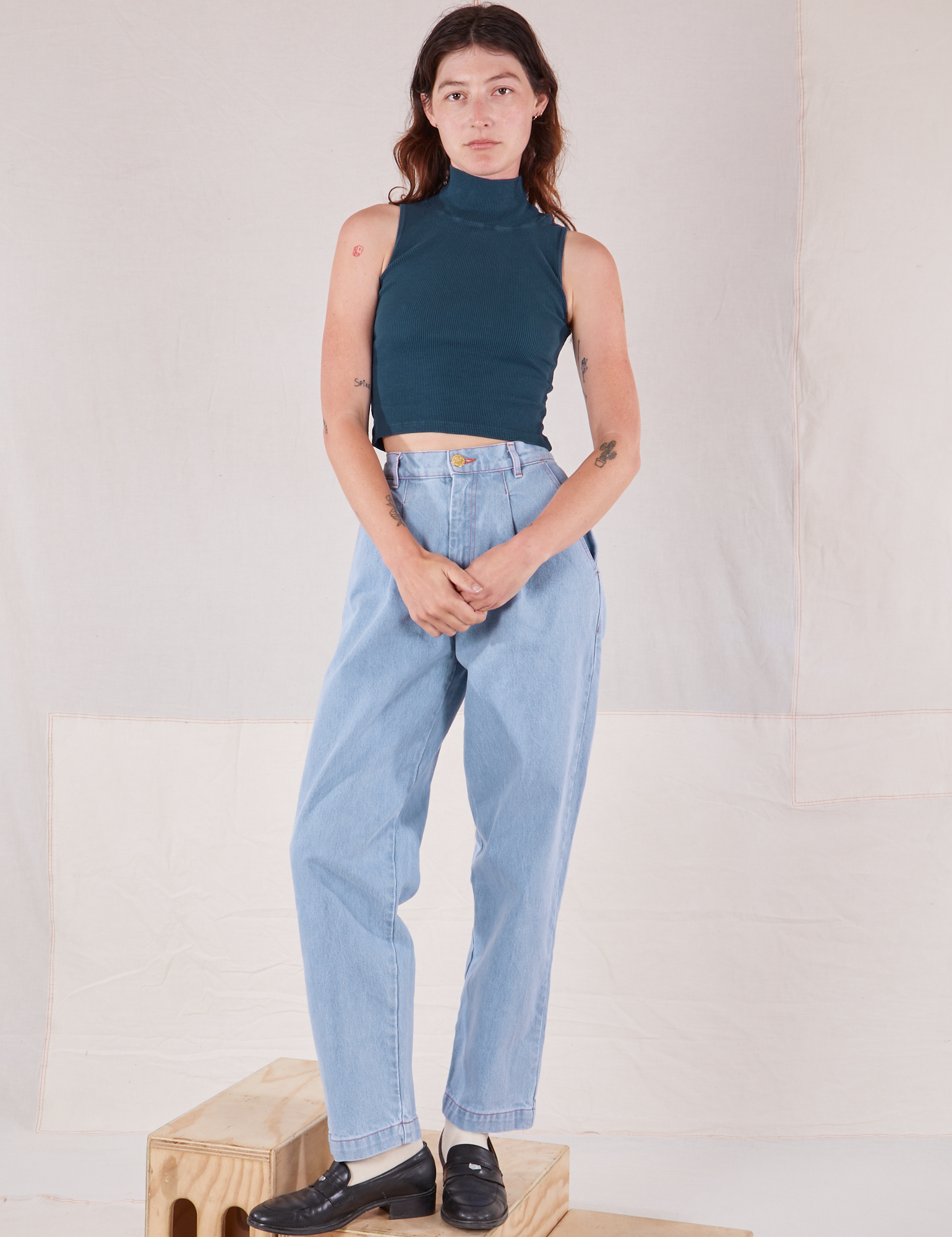 Alex is wearing Sleeveless Essential Turtleneck in Lagoon and light wash Trouser Jeans