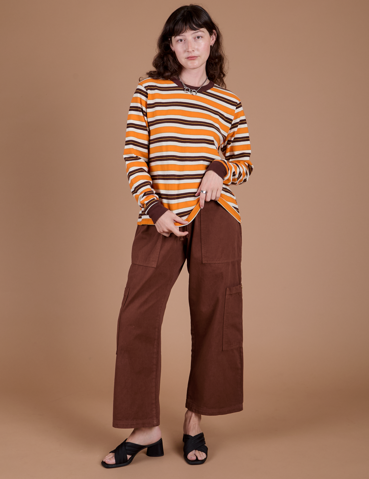 Alex is wearing Long Sleeve Striped Burly Tee in Orange and Drop Pocket Cargo Pants in Fudgesicle Brown