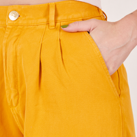 Front pocket close up of Organic Trousers in Mustard Yellow. Alex has her hand in the pocket.