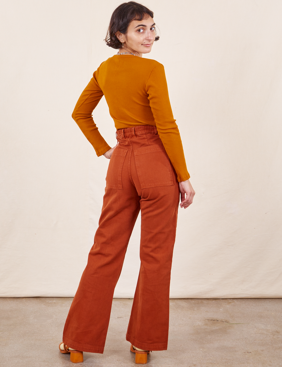 Back view of Western Pants in Burnt Terracotta paired with burnt orange Long Sleeve V-Neck Tee worn by Soraya