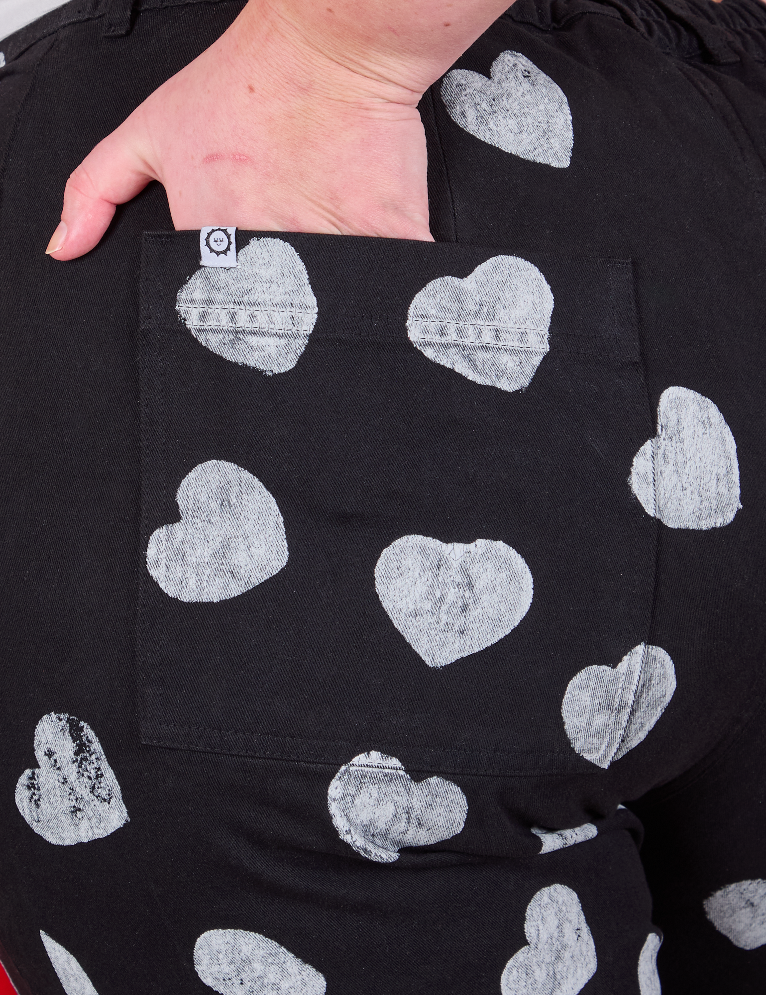 Close up of Juliet&#39;s hand in the back pocket of Paintstamped Heart Work Pants in Black