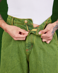 Front close up of Overdyed Wide Leg Trousers in Gross Green. Jesse is pulling on the zipper tab