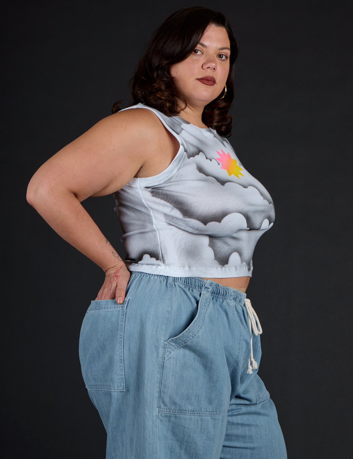 Angled side view of the Dark Cloud Airbrush Muscle Tee and Light Wash Denim Drop Pocket Pants on Kristen
