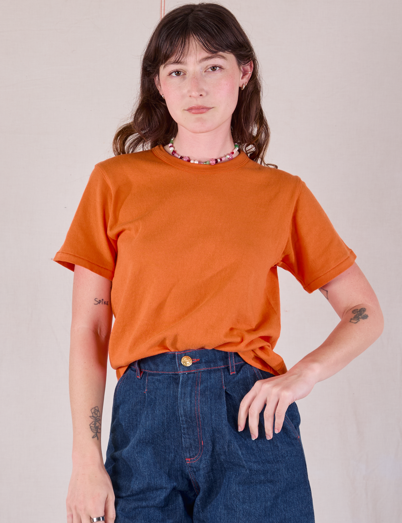 Alex is wearing Burly Tee in Construction Orange tucked into dark wash Denim Wide Leg Trousers