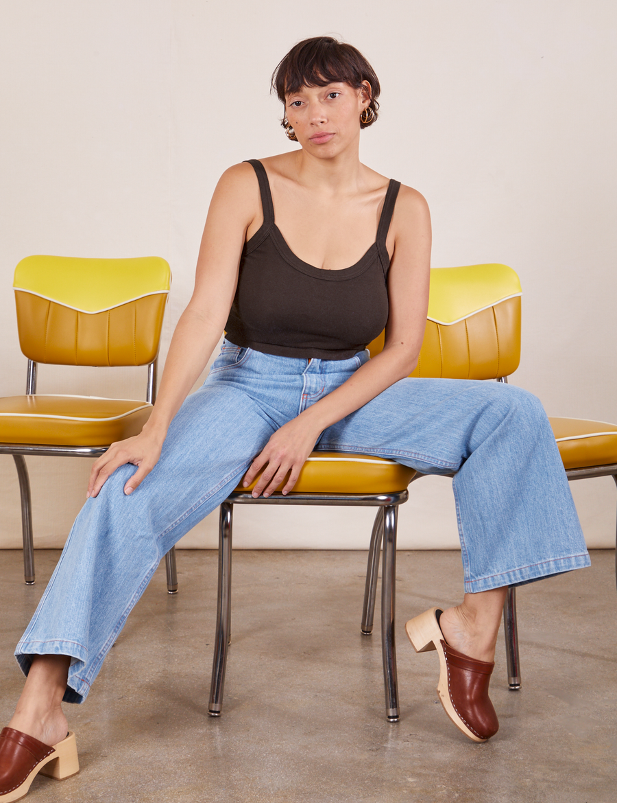 Tiara is sitting on vinyl dining chairs wearing Cropped Cami in Espresso Brown and light wash Sailor Jeans