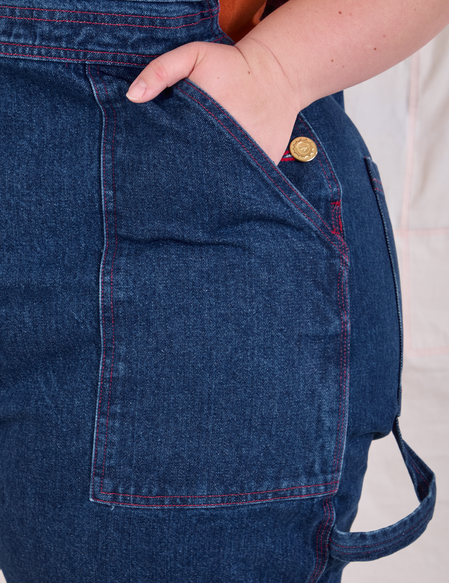 Close up of Ashley&#39;s hand in the front pocket of Carpenter Overalls in Dark Wash